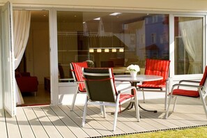 An outdoor patio with a round table and chairs, a glass door leading to a room, and a view of buildings in the background. - House Poseidon - Apartment 1.1 (Wangerooge)