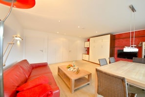 A modern living room with a red sofa, a wooden coffee table, and a dining area with a large table and chairs. - House Poseidon - Apartment 1.1 (Wangerooge)