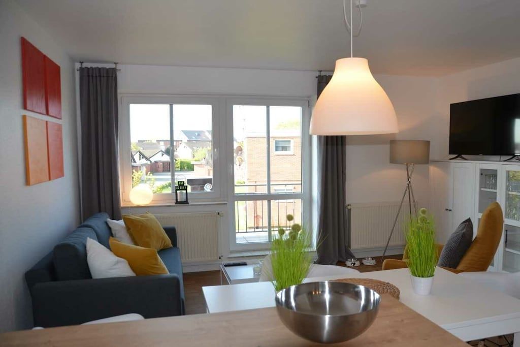 Un salon moderne comprenant un canapé, une table à manger, un téléviseur et une grande fenêtre avec des rideaux.