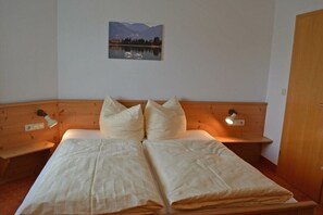 Ein Doppelbett mit zwei Kissen, einer Nachttischlampe und einem Wandbild mit einer Seenlandschaft und Schwänen.