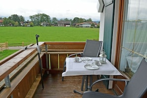 Ein Balkon mit einem Tisch für zwei Personen, der auf ein Wiesenfeld und Häuser blickt.
