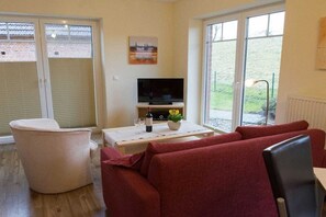 A living room with a sofa, a television, and a table with a bottle and glasses. - Apartment in Jork with swimming pool (Jork)