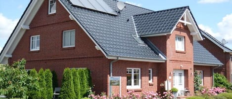 A two-story brick house with a sloped roof, a satellite dish, and a well-maintained garden with shrubs and flowers.