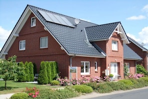 A two-story brick house with a sloped roof, a satellite dish, and a well-maintained garden with shrubs and flowers. - Apartment in Jork with swimming pool (Jork)
