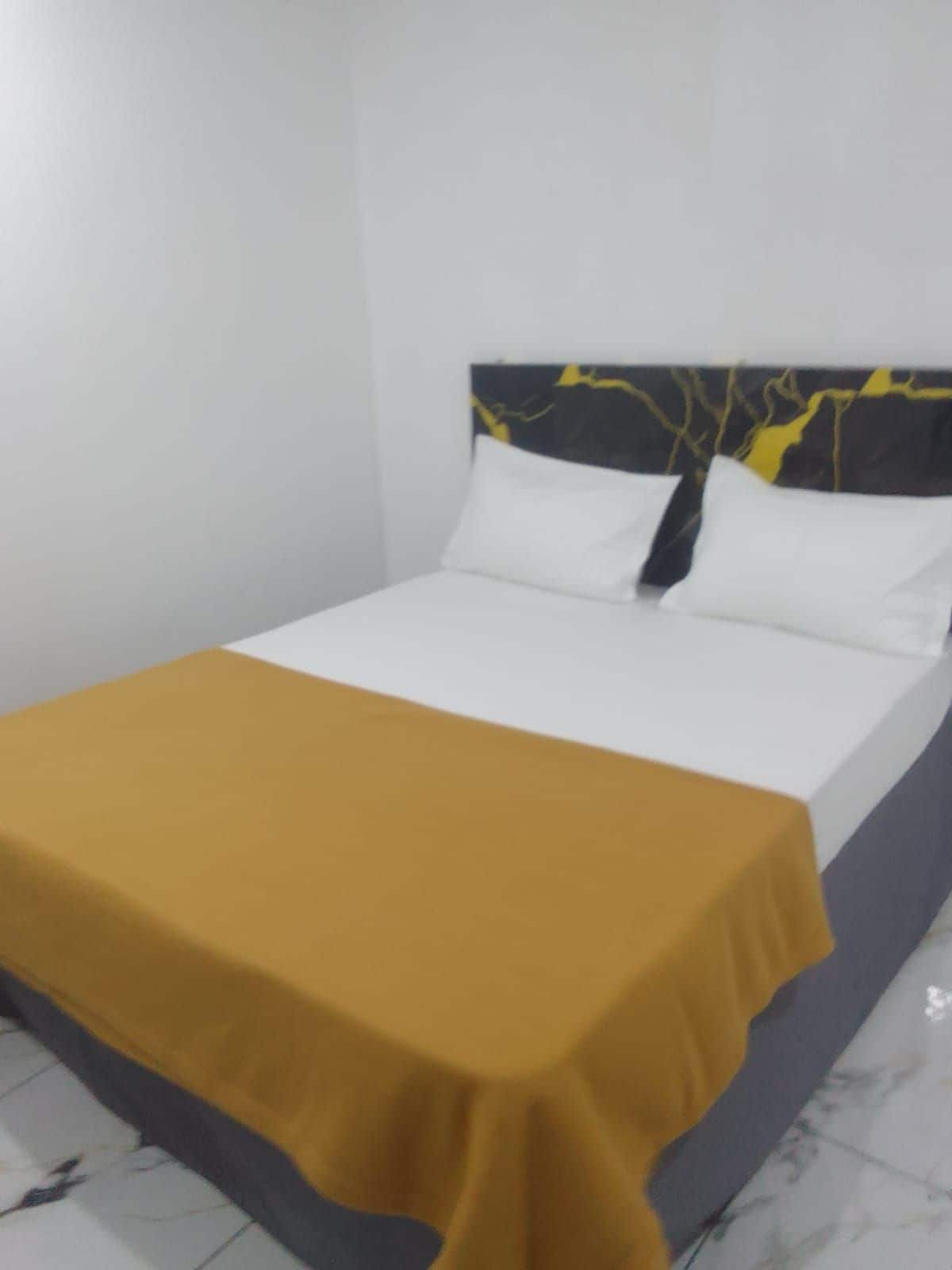 A bed with a white mattress and a mustard-colored bedspread.