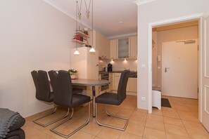 A compact kitchen with modern appliances, a dining area with a table and chairs, and a visible door leading to another room. - Holiday apartment with 1 bedroom (Kühlungsborn)