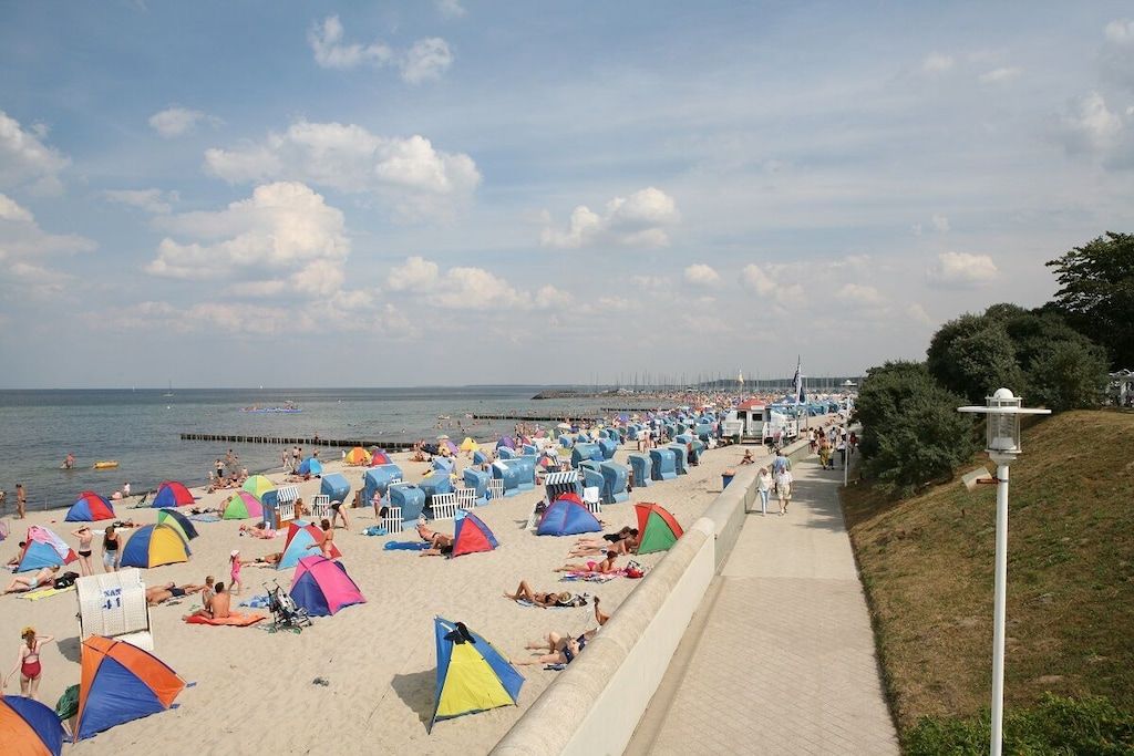Una playa con numerosas tiendas de campaña y sombrillas coloridas, un paseo marítimo y un muelle al fondo.