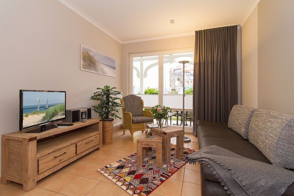 A living room with a TV, wooden furniture, a plant, and a view of the outdoors.