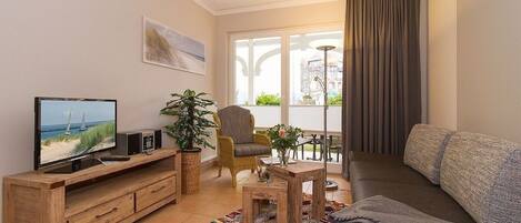 A living room with a TV, wooden furniture, a plant, and a view of the outdoors.