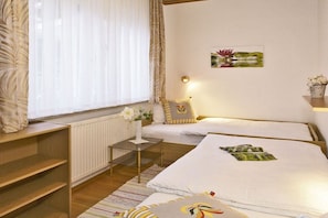A hotel room with two beds, a small table, a radiator, and a window with curtains. - Holiday apartment with 1 bedroom (Ahlbeck)