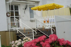 Un bâtiment blanc avec un escalier, un parapluie jaune et des fleurs roses.