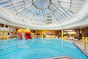 Una piscina interior con techo de vidrio, toboganes y sillas de descanso amarillas.