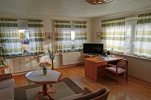 Una sala de estar amoblada con un escritorio de madera, un televisor y una mesa de comedor con un florero.