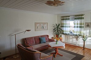 A living room with a sofa, armchair, floor lamp, and a table with a vase of flowers. - Holiday apartment with 1 bedroom (Ahlbeck)