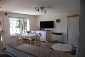 A kitchen with a dining table, chairs, a television, and a clock on the wall. - Holiday home with 1 bedroom (Schwielochsee)