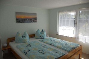 Une chambre à coucher avec un lit, des oreillers, une fenêtre avec des rideaux et un tableau au mur.