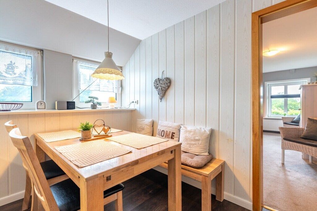 Un coin repas avec une table en bois, des chaises, un luminaire suspendu et une décoration en forme de cœur accrochée au mur.