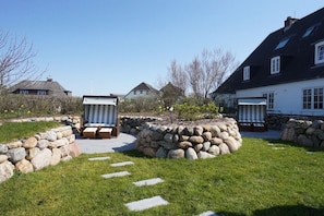 Een tuin met stenen muren, een pad en twee zitplekken buiten.
