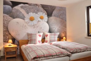 Een slaapkamer met een bed, kussens, een nachtkastje en een muurschildering.