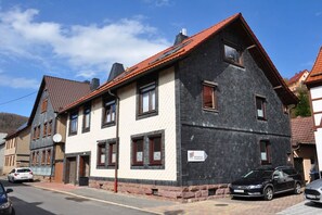 A two-story building with a red-tiled roof, a sign indicating a restaurant, and a parked car in front. - Holiday apartment with 1 bedroom (Steinbach-Hallenberg)