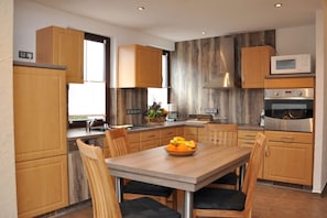 A modern kitchen with wooden cabinets, a built-in microwave, a stainless steel oven, and a dining table with chairs. - Holiday apartment with 1 bedroom (Steinbach-Hallenberg)