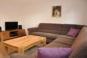 A living room with a brown sofa, a wooden coffee table, a television on a wooden stand, and a framed picture on the wall. - Holiday apartment with 1 bedroom (Steinbach-Hallenberg)