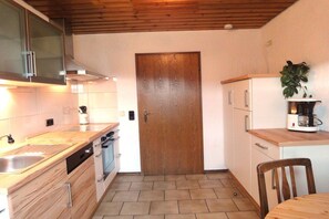 Cocina compacta con puerta de madera, cafetera y zona de comedor con una silla.