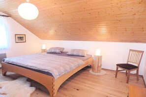 A bedroom with a wooden ceiling, a bed with a knitted blanket, two bedside lamps, and a chair. - Holiday home with 2 bedrooms (St. Georgen\/ Langenschiltach)