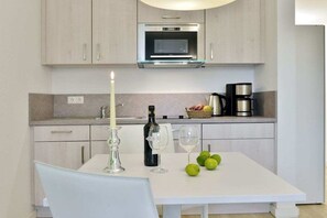 A modern kitchen with a white countertop, a microwave, a coffee maker, and a table with a bottle, glasses, and limes. - Holiday apartment with 1 bedroom (Breege\/Juliusruh OT Juliusruh)