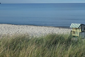 Een strand met een gestreepte strandstoel en een klein gebouwtje, waarschijnlijk een redepost, dicht bij het water.