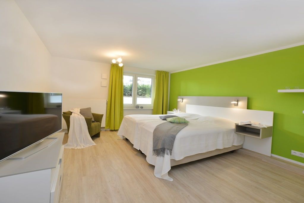 A modern hotel room with a bed, a TV, a desk, and a window with curtains.