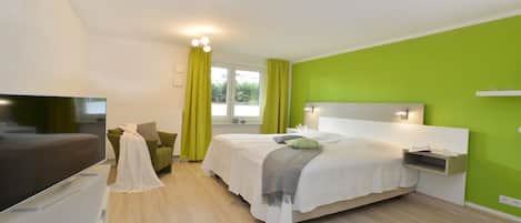 A modern hotel room with a bed, a TV, a desk, and a window with curtains.