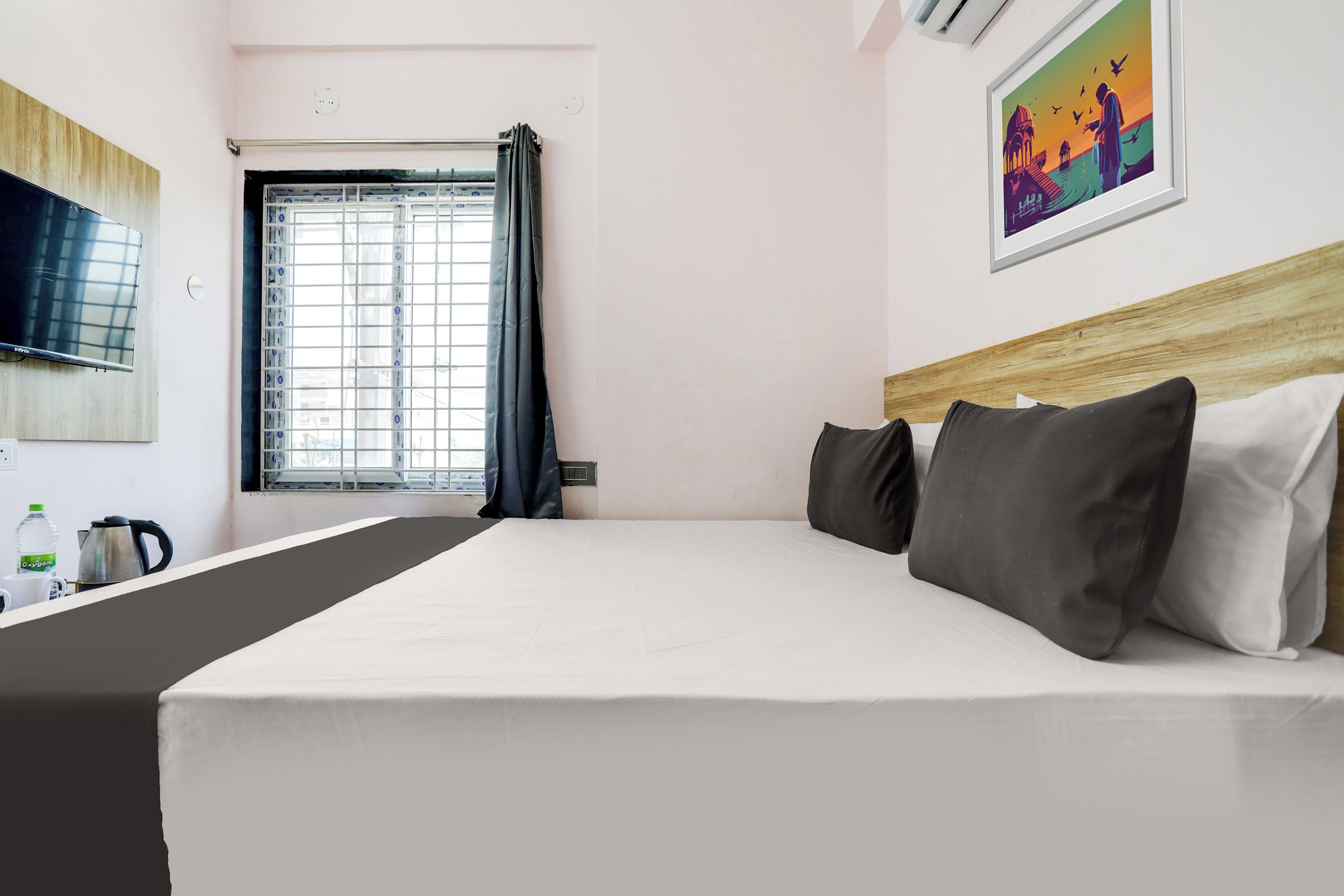 Ein Hotelzimmer mit einem Bett, einem Fernseher, einem Fenster mit Vorhängen und einem Gemälde an der Wand.