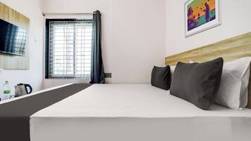 Ein Hotelzimmer mit einem Bett, einem Fernseher, einem Fenster mit Vorhängen und einem Gemälde an der Wand.