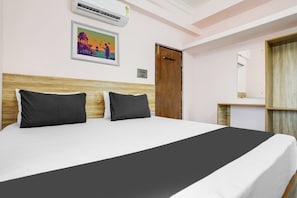 A hotel room with a bed, a wooden headboard, a wall-mounted air conditioner, a framed picture, a door, and a mirror.