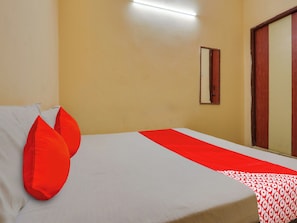 A hotel room with a bed, pillows, a bedside table, a mirror, and a door. - HOTEL O New R Inn (Hyderabad)