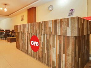 A reception desk with a wooden panel design and a red logo. There are chairs and tables in the background. - HOTEL O New R Inn (Hyderabad)