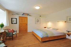 Ein Schlafzimmer mit einem hölzernen Bett, einem Schreibtisch mit Stuhl, einer Holztür und Wandregalen mit Büchern.