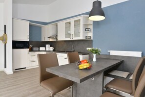 A modern kitchen with white cabinets, a grey countertop, and a dining area with brown chairs. - Holiday apartment with 2 bedrooms (Breege\/Juliusruh OT Juliusruh)