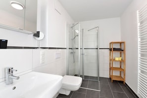 A modern bathroom with a glass-enclosed shower, a white sink, and a wooden shelf. - Holiday apartment with 2 bedrooms (Breege\/Juliusruh OT Juliusruh)