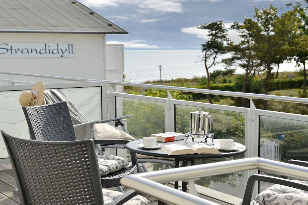 A balcony with wicker furniture, a table with a book and a cup, and a view of the sea.