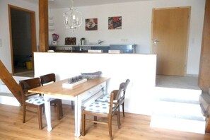 A dining area with a wooden table and chairs, a kitchen in the background, and a staircase leading to an upper level. - Baltic Sea Holiday Farm Sandmann (Hansühn)