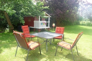 A patio area with a metal table and four chairs, surrounded by grass and trees. - Baltic Sea Holiday Farm Sandmann (Hansühn)
