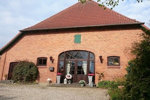 A brick building with a pitched roof, a large arched entrance, and a small green window above the door. - Baltic Sea Holiday Farm Sandmann (Hansühn)