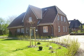 A two-story brick house with a sloped roof, a front garden with a wooden pergola, and a paved driveway. - Holiday apartment in Föhr with 1 bedroom (Oldsum)