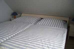 A bedroom with a bed, two pillows, a nightstand, and a lamp. - Holiday apartment in Föhr with 1 bedroom (Oldsum)