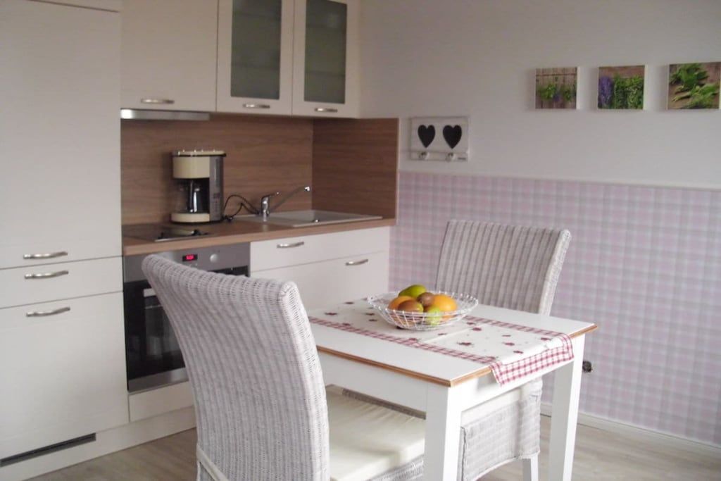 A kitchen with a white table, two chairs, a coffee maker, and a fruit bowl.