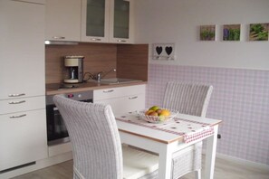 A kitchen with a white table, two chairs, a coffee maker, and a fruit bowl. - Holiday apartment in Föhr with 1 bedroom (Oldsum)