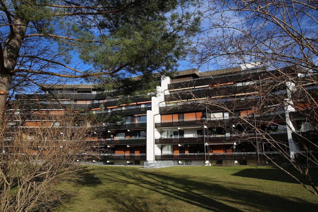 A multi-story residential building with balconies, a central white pillar, and a grassy courtyard.