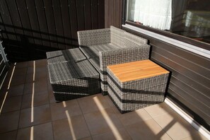 A wicker sofa and a wooden coffee table on a tiled floor, positioned near a window with blinds. - Holiday apartment with 1 bedroom (Füssen)